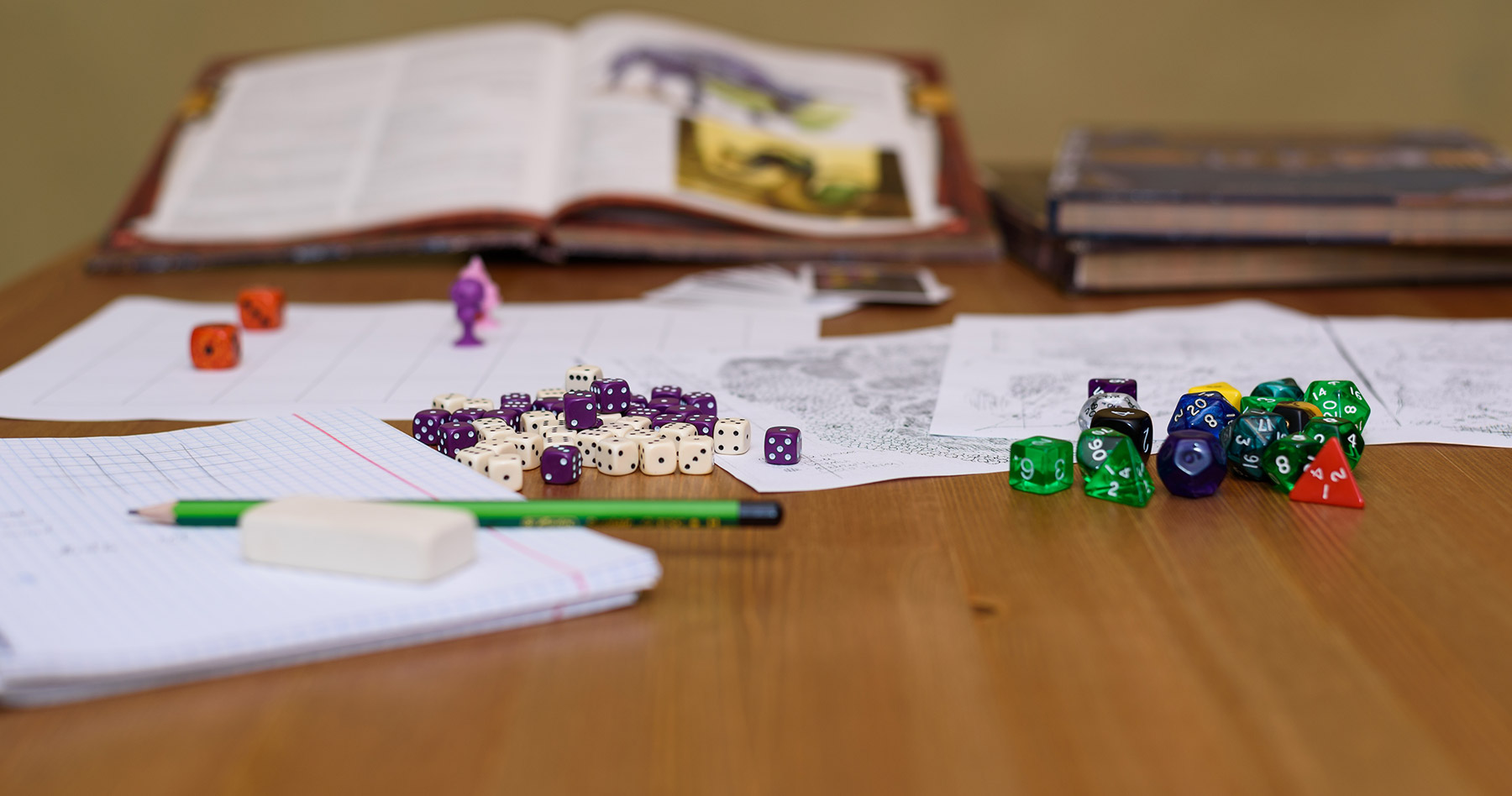 A tabletop scene featuring colorful dice, stacked books, and a sharpened pencil arranged neatly.